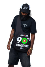Person wearing a black t-shirt with 'Bad Like 90s Dancehall' design, black cap, and dark shorts on a white background.  Cooyah Clothing brand.  We are a Jamaican owned clothing brand since 1987.