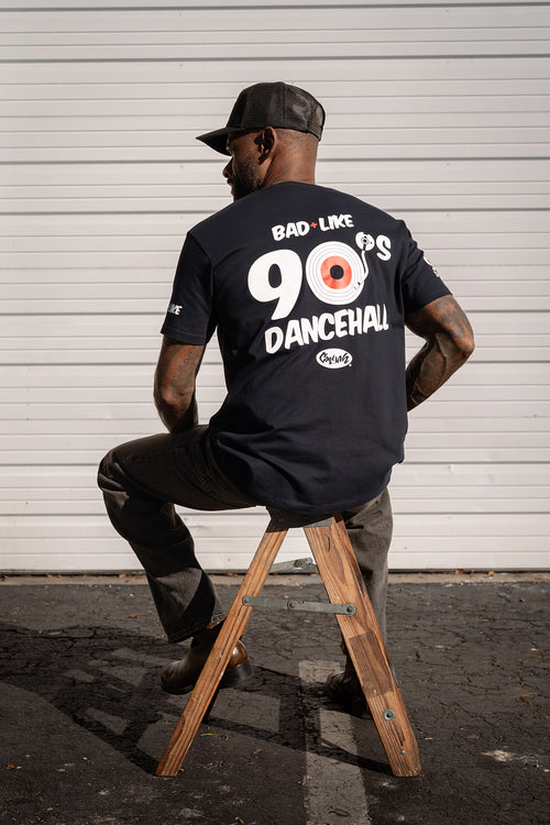 Back view of model wearing Cooyah Bad Like 90s Dancehall graphic t-shirt, featuring bold reggae-inspired back print. We are a Jamaican owned clothing brand established in 1987.