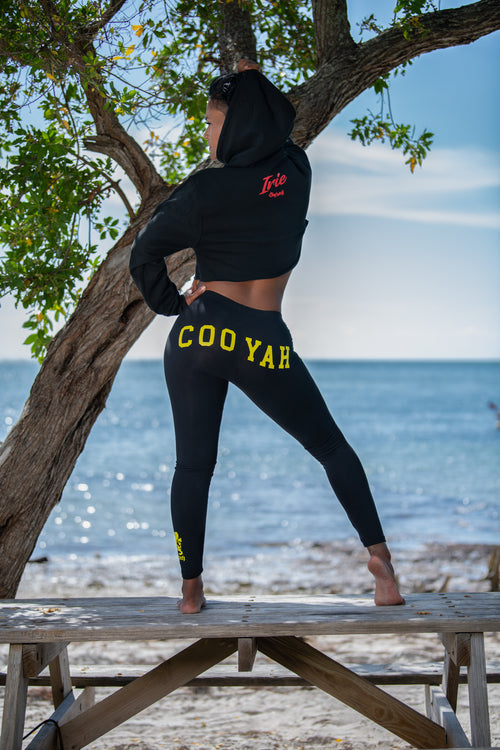 Model wearing a cropped black hoodie and leggings with 'COOYAH' text on a beach.