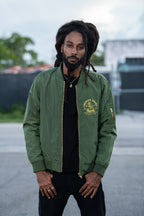 Cooyah Premium Brand bomber jacket with a gold lion graphic on the chest. Model standing outdoors in an urban setting. The jacket features a front zipper, ribbed cuffs and hem, and a sleeve zip pocket.