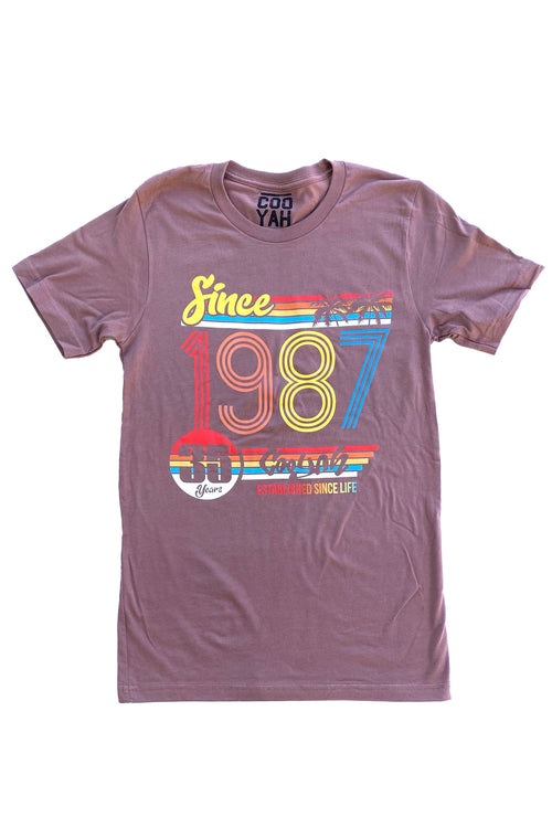 Cooyah Clothing 1987 Anniversary men's graphic tee in brown. As a Jamaican owned clothing brand since 1987, we take pride in bringing you this classic piece. Don't wait, get yours now!