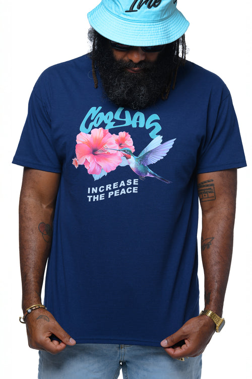 Man wearing a dark blue Cooyah t-shirt with a hummingbird and hibiscus flower graphic design and text, 'Increase the Peace' standing against a white background