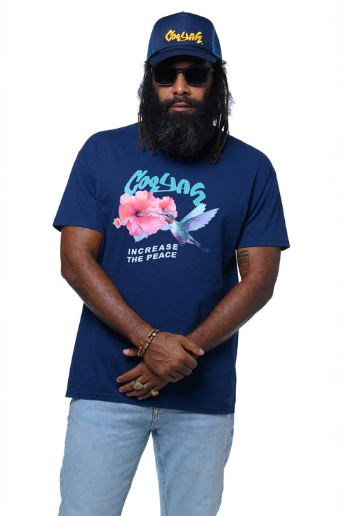 Man wearing a navy blue Cooyah t-shirt with a hummingbird and hibiscus flower graphic design and text, 'increase the peace' standing against a white background.