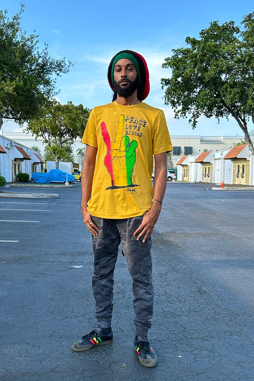 Peace Love Reggae graphic t-shirt by Cooyah Clothing featuring a colorful red, yellow, and green hand peace sign design on a mustard yellow shirt. Vintage ’70s reggae-inspired artwork promoting positivity, unity, and good vibes.