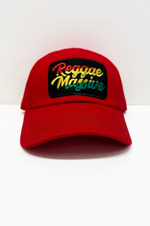 A red baseball cap with a black rectangular embroidered patch on the front that reads 'Reggae Massive' in a gradient of red, yellow, and green, set against a plain white background. Cooyah Clothing Brand.