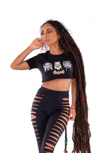 Woman wearing a black crop top with graphic designs and black ripped leggings on a white background