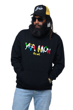 Man wearing a black hoodie with colorful text 'Yea Mon' and Cooyah logo, light blue jeans, and a black and yellow cap with 'Irie" embroidery.