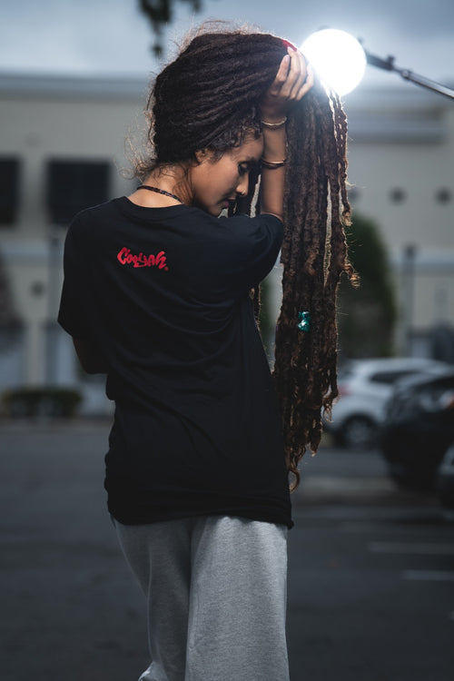 Rasta woman with locs wearing a black t-shirt with Cooyah logo on the back.