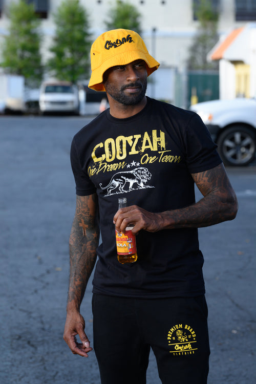 Cooyah Jamaica. One Dream, One Team, men's graphic tee in black with metallic gold lettering and white lion print.