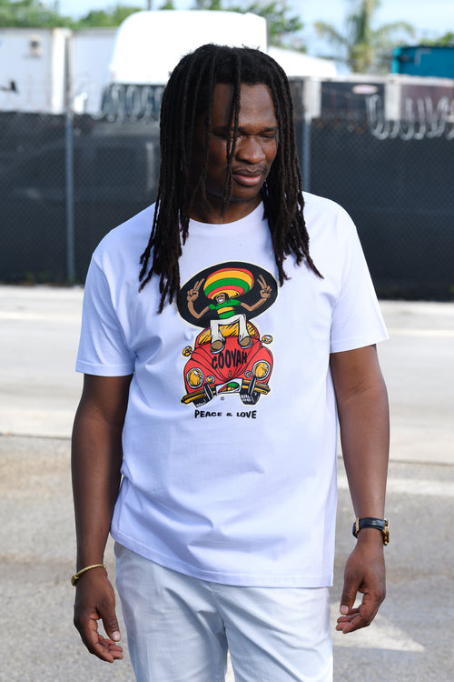 Reggae Singer Kumar Fya in a Cooyah graphic t-shirt featuring a rasta cartoon character on a red VW Beetle Car with the text 'COOYAH' and 'PEACE = LOVE' below it, paired with white pants in an outdoor setting.