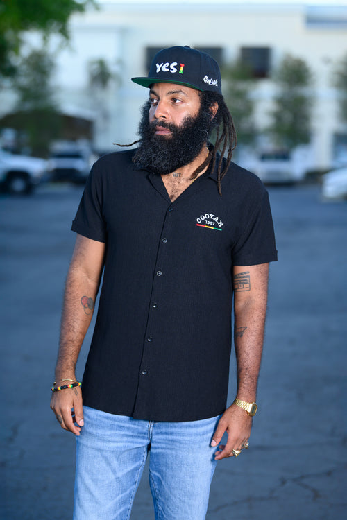 Men's black snapback hat with Yes I embroidered graphic in reggae colors.