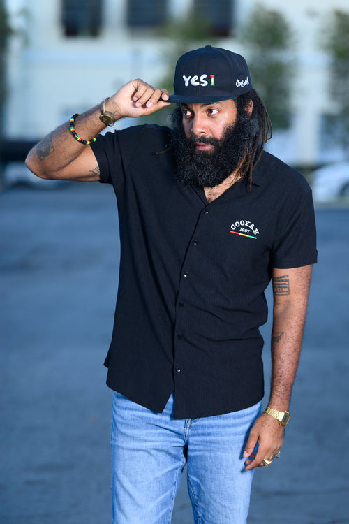 Men's black snapback hat with Yes I embroidered graphic in reggae colors.