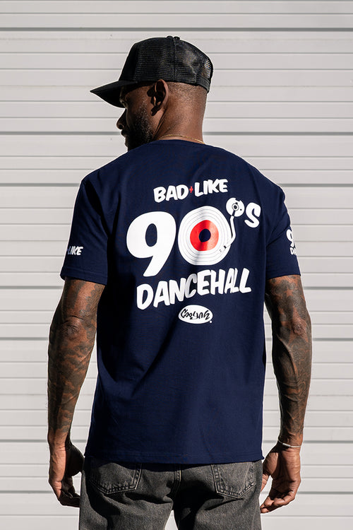 Man wearing a navy blue t-shirt with 'Bad Like 90s Dancehall' text and record design on the back, standing against a gray background.  Cooyah, Jamaica's leading clothing brand since 1987.