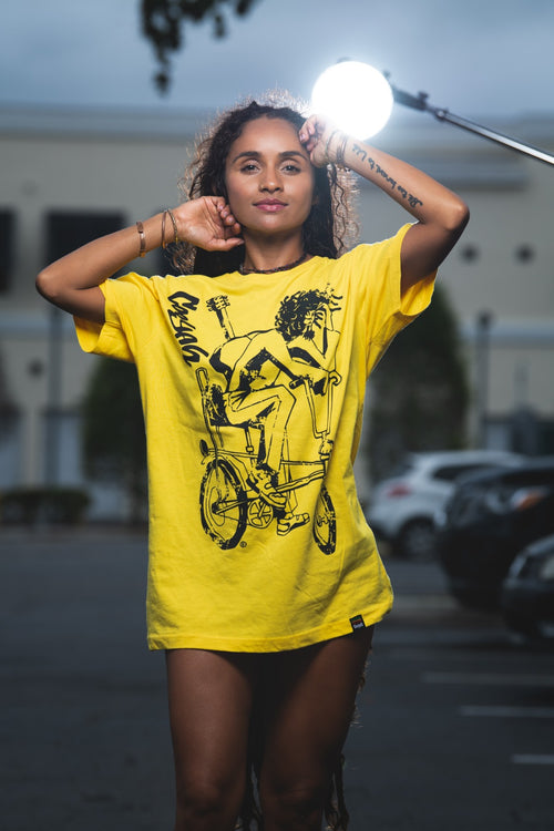 Cooyah Jamaica. Women's relaxed fit Simmer Down T-Shirt featuring a Rastaman on a bicycle design. Ring Spun Cotton, Short Sleeve yellow Tee. Jamaican streetwear clothing brand.