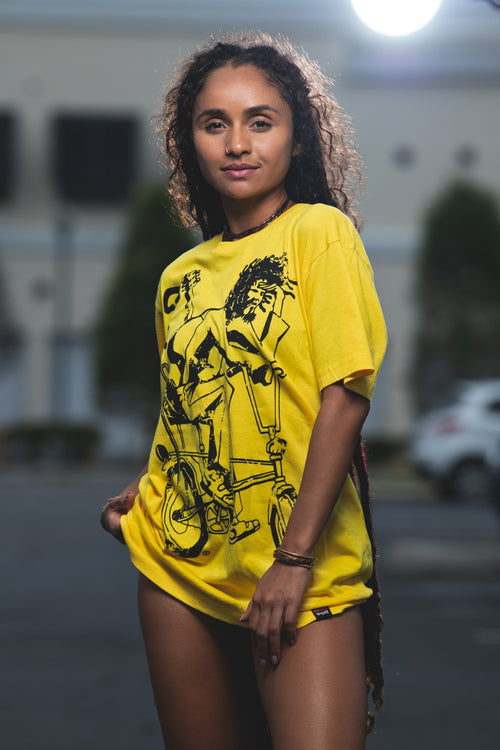 Cooyah Jamaica. Women's relaxed fit Simmer Down T-Shirt featuring a Rastaman on a bicycle design. Ring Spun Cotton, Short Sleeve yellow Tee. Jamaican streetwear clothing brand.