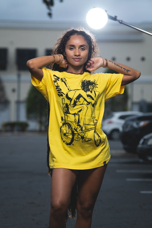 Cooyah Jamaica. Women's relaxed fit Simmer Down T-Shirt featuring a Rastaman on a bicycle design. Ring Spun Cotton, Short Sleeve yellow Tee. Jamaican streetwear clothing brand.